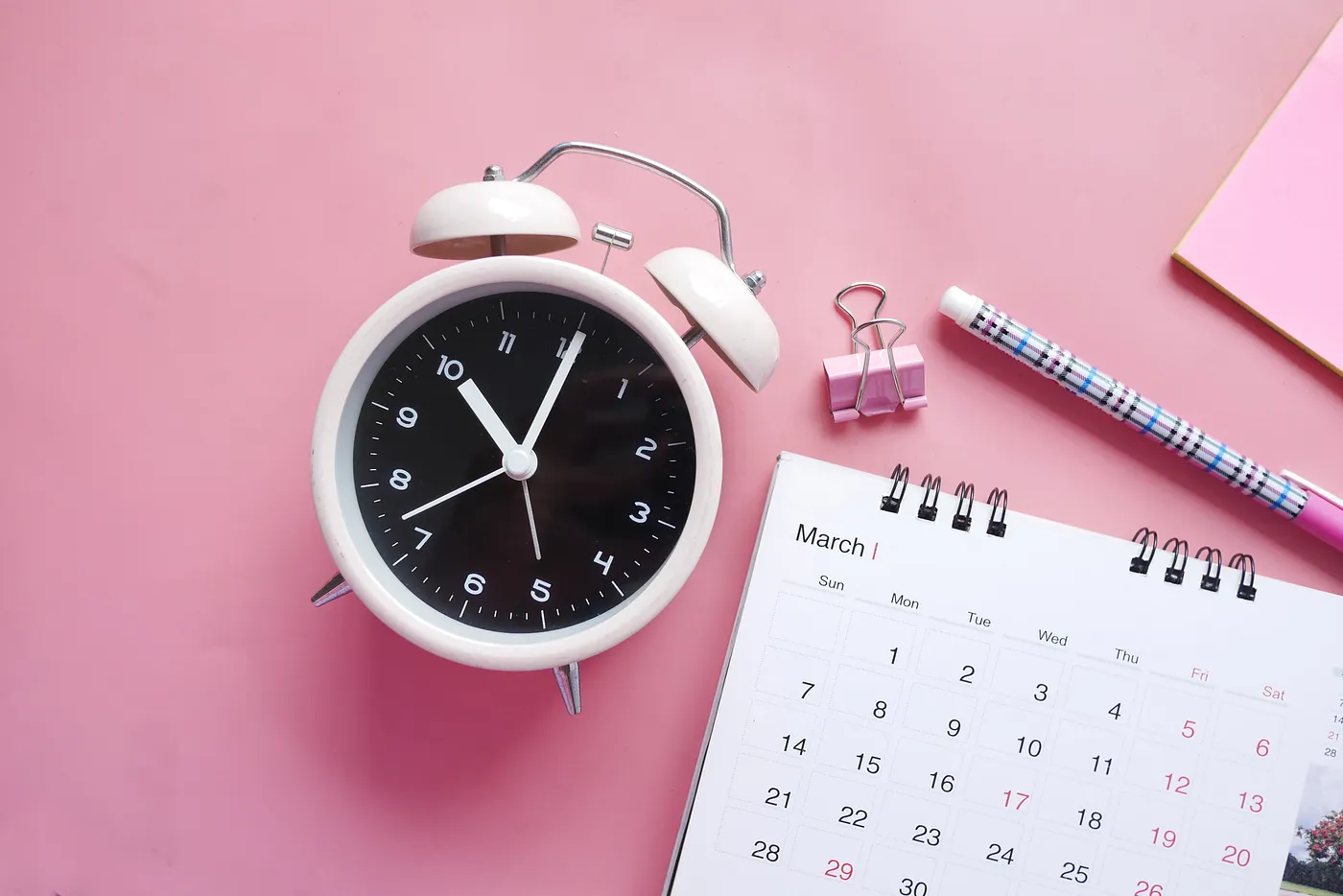 a clock, calendar, and stationery on top of a pink background